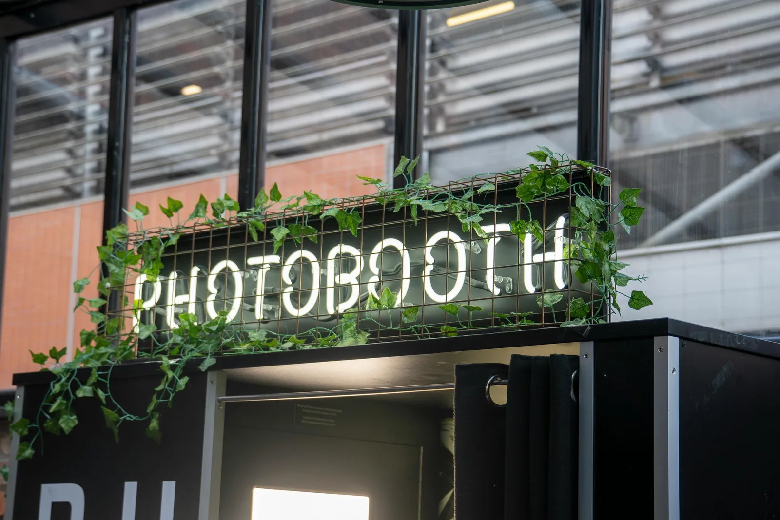 A modern Look at You photo booth with a neon PHOTOBOOTH sign and trailing greenery